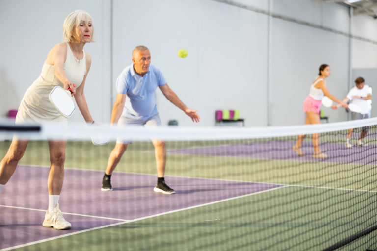 Elderly woman playing pickleball match in team with male partner